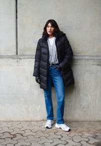 Čierna ajfková bunda, sivý kardigán, biele tričko, modré džínsy a biele tenisky. Hladké textúry, kapucňový dizajn, priliehavý strih, ležérny vzhľad.