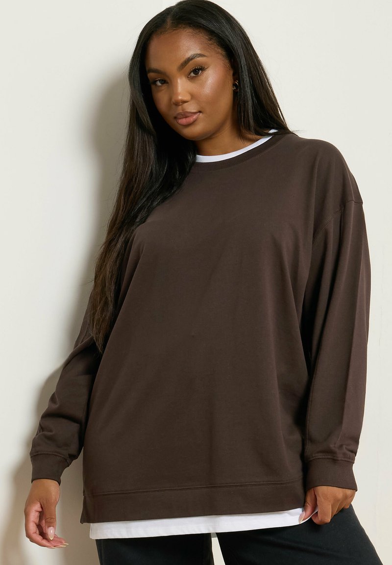 Brauner übergroßer Sweatshirt mit langen Ärmeln, rundem Halsausschnitt und weißem Hemdsaumdetail. Weicher Stoff und minimalistisches Design.
