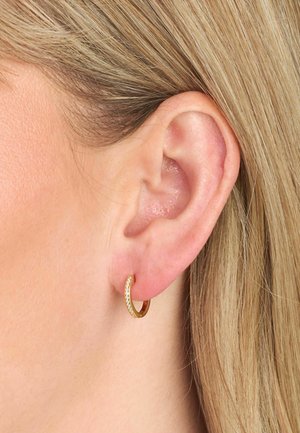 Zelta stīpas auskari ar teksturētu virsmu un spožu apdari. Dizains ir mazs un apļveida, cieši pieguļ ausu ļipiņai.