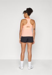 Athletic tank top in bright orange with a racerback and cutout detail, paired with black shorts. White ankle socks and gray shoes.
