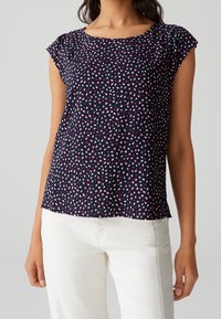 Blouse bleu marine à manches courtes et col rond, présentant un motif dispersé de points roses et blancs sur un tissu lisse.