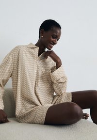 Hellbeiges Hemdkleid mit geometrischem Muster, knopfähnlichem Design, lässiger Silhouette und langen Ärmeln. Weicher Stoff mit strukturierter Optik.