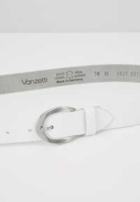 Hvit lærbelte med en sølv metallisk oval spenne. Har små hull for størrelsesjustering og merking av merket på innsiden. Laget i Tyskland.