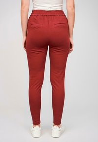 Bordové legíny so slim fit strihom, vyrobené z mäkkej tkaniny, s elastickým pásom a dvoma zadnými vreckami. Nosené s bielymi teniskami.