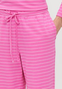 Ružové pyžamové nohavice majú jemnú textúru s vodorovnými bielymi pruhmi, elastický pás a šnúrku na prispôsobenie veľkosti.