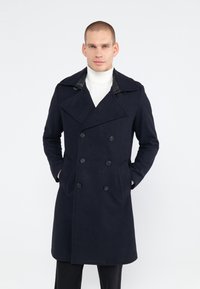 Marineblauwe dubbele-breasted wollen jas met een geknipte kraag, leren accenten op de kraag, zijzakken en een recht model.