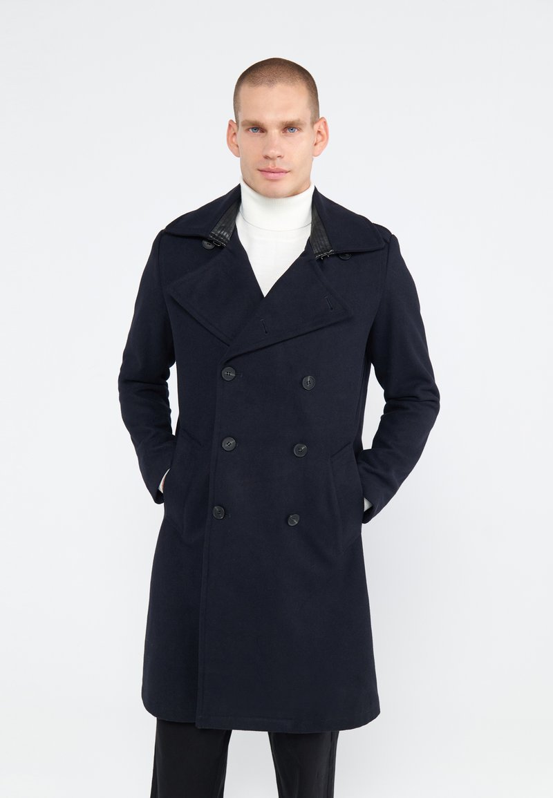 Marineblauwe dubbele-breasted wollen jas met een geknipte kraag, leren accenten op de kraag, zijzakken en een recht model.