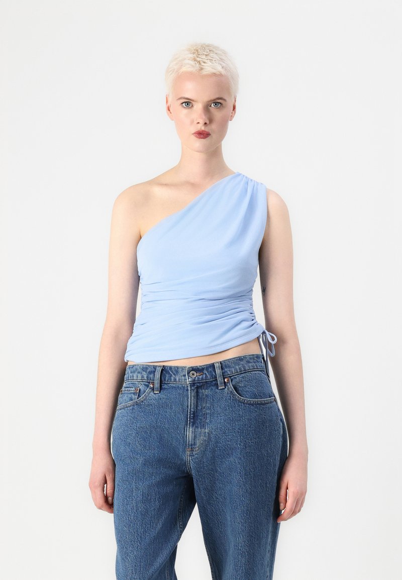 Lichtblauwe, one-shoulder top met een gerimpeld ontwerp; zachte, gladde textuur. Gecombineerd met high-waisted, ontspannen spijkerbroek.