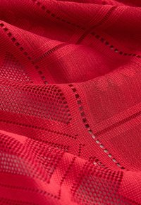 Red fabric with alternating solid and mesh square patterns, showing a textured knit and small holes in a geometric grid design.