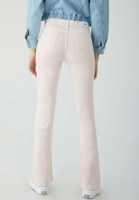Vaqueros de campana rosa claro con bolsillos traseros y costuras en contraste, combinados con zapatillas blancas. Tejido de denim con textura suave.