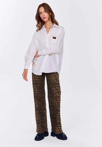Biała koszula z guzikami z ozdobnym haftem, zestawiona z brązowymi spodniami w panterkę o szerokich nogawkach i czarnymi masywnymi botkami.