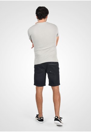 Harmaa lyhythihainen t-paita, jossa on pesty leikkaus, yhdistetty tummiin farkkushortseihin, joissa on käännetyt hihat, ja mustiin tennareihin, joissa on valkoiset pohjat.