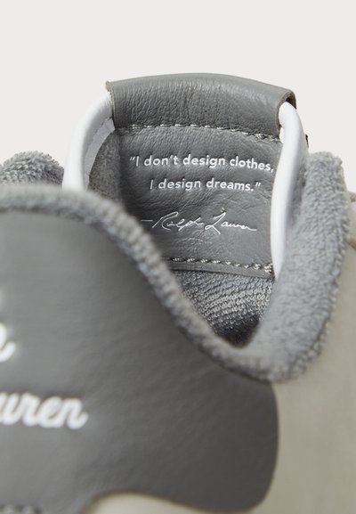 Sivé kožené topánky s mäkkou sivou textíliou vo vnútri. Interiér obsahuje citát vytlačený bielou farbou na textúrovanom sivom pozadí.