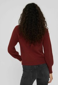 Pull en tricot bordeaux avec des manches texturées, un ourlet côtelé et un design épuré, associé à un jean noir ajusté.