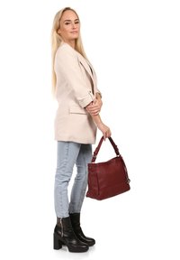 Beige blazer met opgerolde mouwen, lichtblauwe jeans, zwarte platformlaarzen en een gestructureerde rode handtas met schouderband.