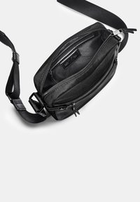Černá crossbody taška vyrobená z látky, s kapsami na zip, nastavitelným popruhem a hladkým vnitřním podšívkou. Obsahuje minimální kovové detaily.