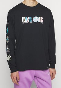 Svart långärmad t-shirt med flerfärgad "NIKE AIR" logotyp på framsidan, grafiska mönster på ärmarna och rundad halsringning.