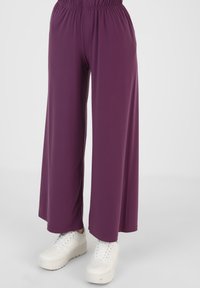 Paarse wijde broek gemaakt van een gladde, lichte stof met een elastische tailleband, gecombineerd met witte sneakers.