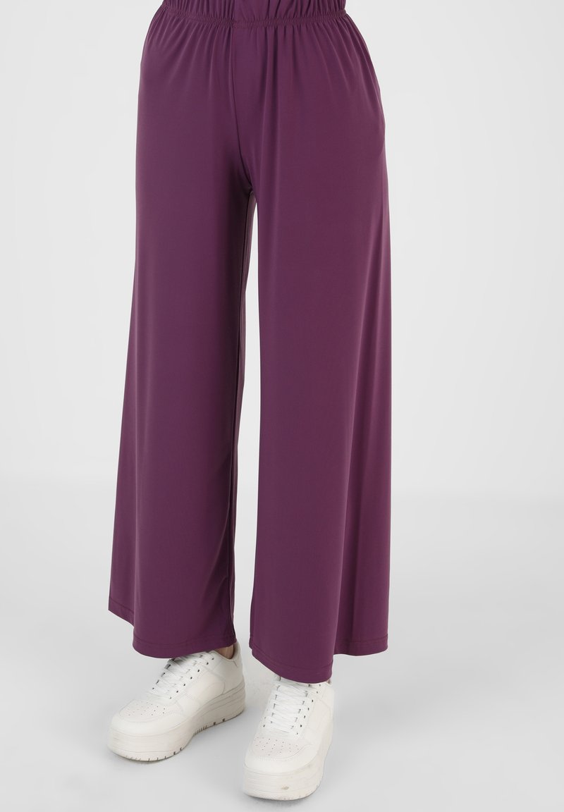 Paarse wijde broek gemaakt van een gladde, lichte stof met een elastische tailleband, gecombineerd met witte sneakers.