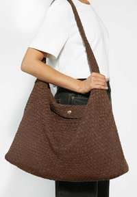 Brown woven shoulder bag with a textured, hobo design. Features a snap closure and a wide, braided strap for easy carrying.