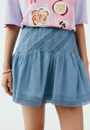 Jupe bleu clair en tissu texturé, avec un ourlet froncé et des accents en dentelle. Présente des motifs de couture diagonaux et une taille froncée.