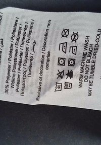 Hvit tekstilpleieetikett med svart tekst som indikerer materialkomposisjon: 30% polyester. Symboler for vask, tørking og pleieinstruksjoner.