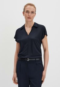 Blouse bleu marine à manches courtes avec un col et un décolleté en V. Texture lisse, coupe légèrement ample. Associée à un pantalon bleu marine taille haute et une ceinture noire.