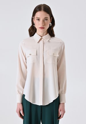 Helles rosa Langarmshirt mit spitzem Kragen, zwei Brusttaschen und Knopfdetails. Glattes Material mit leicht abgerundetem Saum.