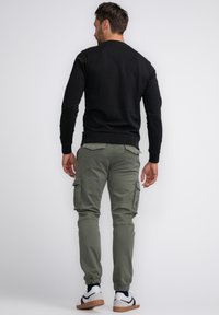 Zwarte sweatshirt met lange mouwen gecombineerd met olijfgroene cargo-broek met zijzakken en elastische manchetten, aangevuld met witte en bruine sneakers.