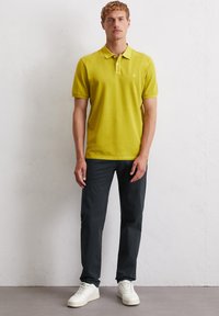 Koszulka polo w jasnym żółtym kolorze z kołnierzykiem, krótkimi rękawami i subtelnym logo, w połączeniu z ciemnymi spodniami i białymi trampkami.
