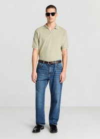 Polo vert clair avec bordure blanche, jean en denim bleu et chaussures noires. Des lunettes de soleil complètent la tenue décontractée.