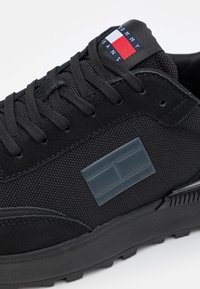 Sneakers nere in mesh e suede, con lacci piatti, suola in gomma e logo "TOMMY JEANS" in rilievo sul lato.