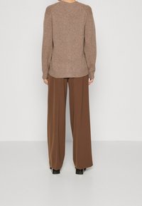 Brązowy sweter z dzianiny z prążkowanymi detalami na ramionach, zestawiony z szerokimi brązowymi spodniami o luźnym kroju i czarnymi botkami na blokowanym obcasie.