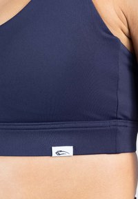 Sujetador deportivo azul marino hecho de un tejido suave, con una banda ancha y una pequeña etiqueta blanca con un logo negro en la parte inferior.