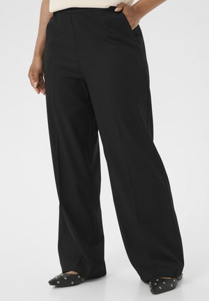 Schwarze weit geschnittene Hosen aus einem glatten Stoff mit Seitentaschen und taillierter Passform. Getragen mit schwarzen spitzen Ballerinas, die mit silbernen Akzenten verziert sind.