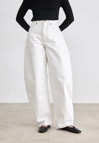 Witte high-waisted, wijde broek van denim, met voorzakken en contrasterende stiksels. Gestyled met zwarte platte schoenen.