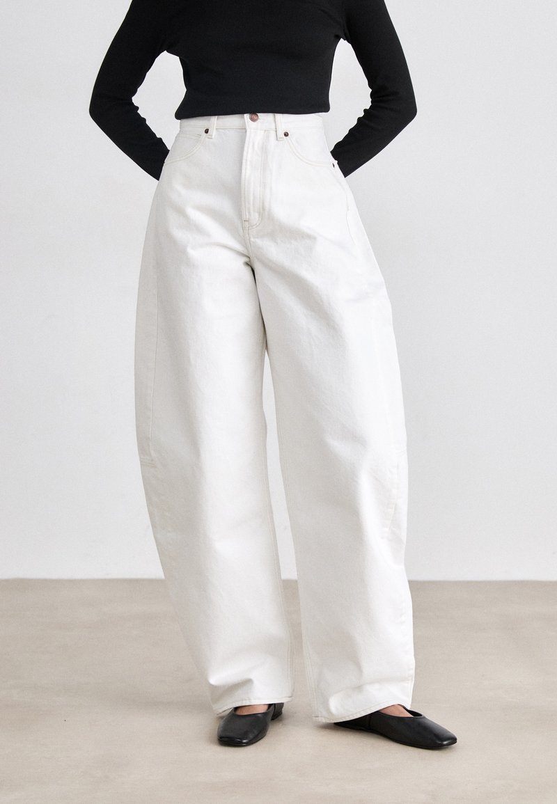 Witte high-waisted, wijde broek van denim, met voorzakken en contrasterende stiksels. Gestyled met zwarte platte schoenen.
