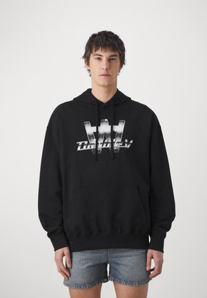 Black hoodie with a large metallic silver logo on the front, featuring a drawstring hood and a kangaroo pocket. Worn with denim shorts.