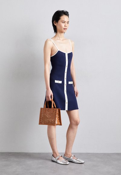 Vestido de marina con detalles en blanco, botones y bolsillos; combinado con un bolso perforado beige y zapatos plateados. Diseño corto y ajustado.