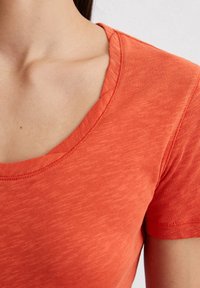 Lyhythihainen T-paita teksturoidusta korallikankaasta, jossa on pyöreä pääntie ja vartalonmyötäinen design. Saumadetailit ovat hillittyjä.