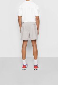 Ljust grå, mönstrade shorts med elastisk midja och en dragkedjeficka på baksidan, tillsammans med en vit kortärmad skjorta och träningsskor.