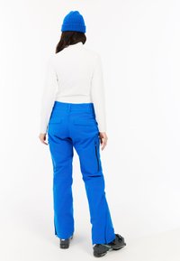 Blauwe sneeuwbroek van waterdicht materiaal, met ritsen aan de zijkanten en meerdere zakken. Graag gecombineerd met een witte lange mouwen top en een blauwe beanie.