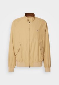 Veste beige zippée avec col montant, poches à rabat boutonnées, poignets et ourlet côtelés, présentée sur un fond uni.