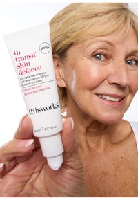 Weisse Tube der "thisworks in transit skin defence" Feuchtigkeitscreme, 40 ml, mit pinker Schrift. Verfügt über eine Pumpdüse und ein SPF 50+ Etikett. Glatte Textur.