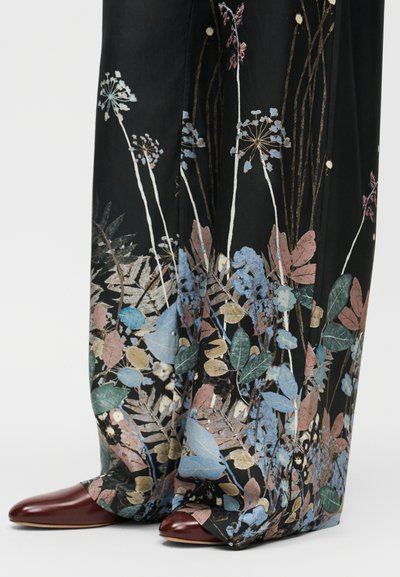 Μαύρο ύφασμα παντελόνι με λουλουδάτο σχέδιο σε μπλε, ροζ, πράσινο και μεταλλικές πινελιές. Μπορντό παπούτσια με μυτερή μύτη.