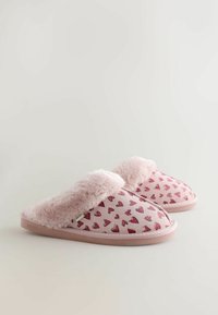 Roze pantoffels met een zachte vachtrand, voorzien van een hartjespatroon op zacht materiaal. Platte zool met een subtiel merkembleem aan de zijkant.