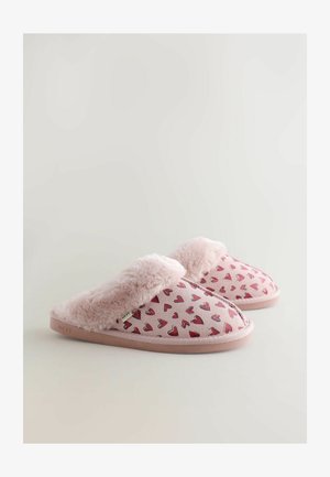 Rosa tofflor med fluffig pälsdetalj och hjärtmönster på mjukt material. Platt sula med en diskret varumärkesetikett på sidan.