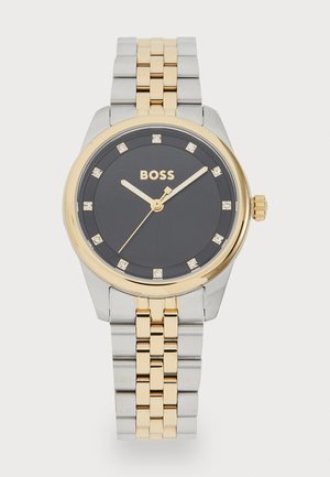 Montre en or et argent avec un cadran rond noir, présentant des index d'heure en forme de diamants, et un bracelet en métal à maillons.