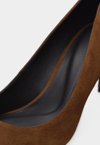 Κοντινή λήψη καφέ σουέντ γόβας με ψηλό τακούνι που δείχνει την ομαλή μαύρη εσωτερική σόλα και το μυτερό σχέδιο μύτης.