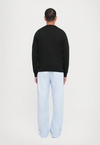 Svart hettegenser med rund halslinning og ribbestrikket kant, kombinert med blå stripete vide bukser. Stoffet ser mykt og teksturert ut.